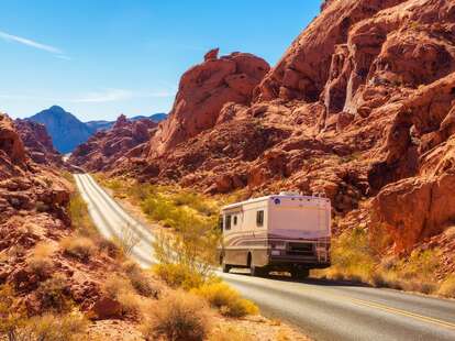 An RV drives between rock formations in the Nevada desert.