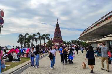 Visitors wander a cloudy boardwalk with a large Christmas Tree in the background.