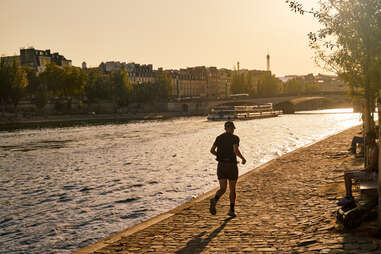 a jogger runs along the bank of the seine river in paris, france at sunset
