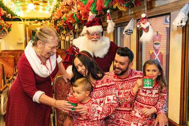 Santa and Mrs. Claus with a family dressed in holiday pajamas.