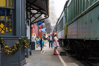 A woman dressed as a Christmas elf waits on a train platform.