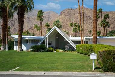 a mid-century modern home with a grass lawn under an array of palm trees in front of the mountains in palm springs, ca