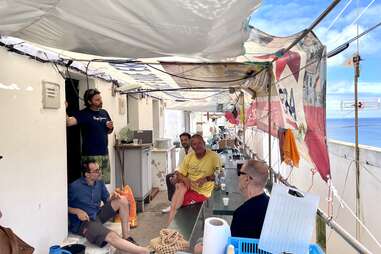 a group of men sitting on a patio, the sea in the background