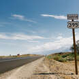 a road sign that says South 395 on a strip of dusty gravel next to an asphalt highway under blue skies in California